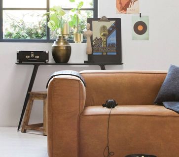 Lysbrun sofa forran et svart bord med blomster og bilde