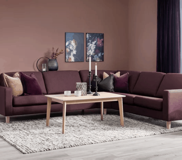 Mørkerød sofa, lyst kaffebord og to bilder på veggen